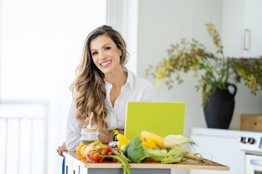 Cici McGuane smiling in her kitchen beside fresh produce and a chartreuse laptop