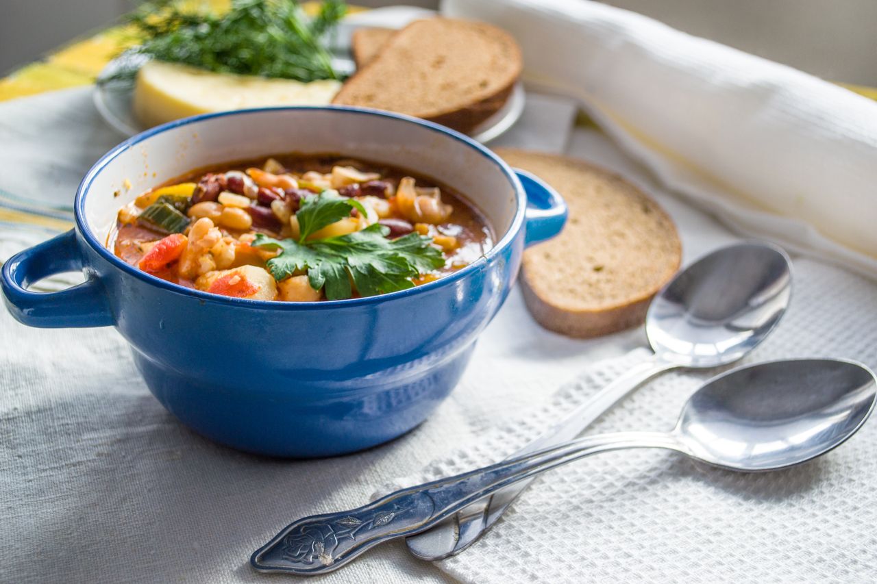 Colorful vegetable soup in a blue ceramic bowl with slices of bread on a table
